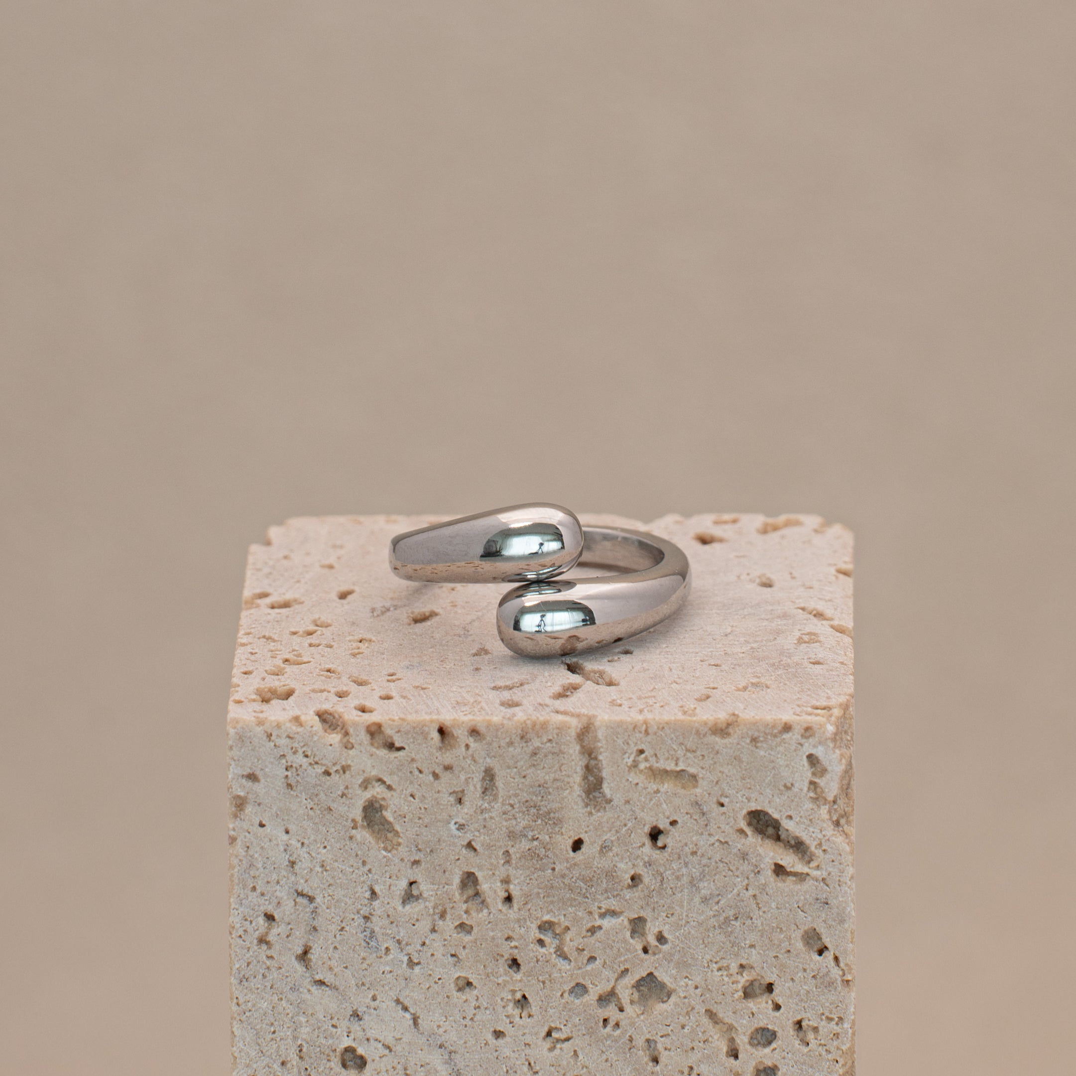 Amar Ring in silber mit zwei tropfenférmigen Enden, liegend auf einem Stein.