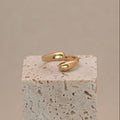 Amar Ring in gold mit zwei Tropfenförmigen Enden, liegend auf einem Stein.
