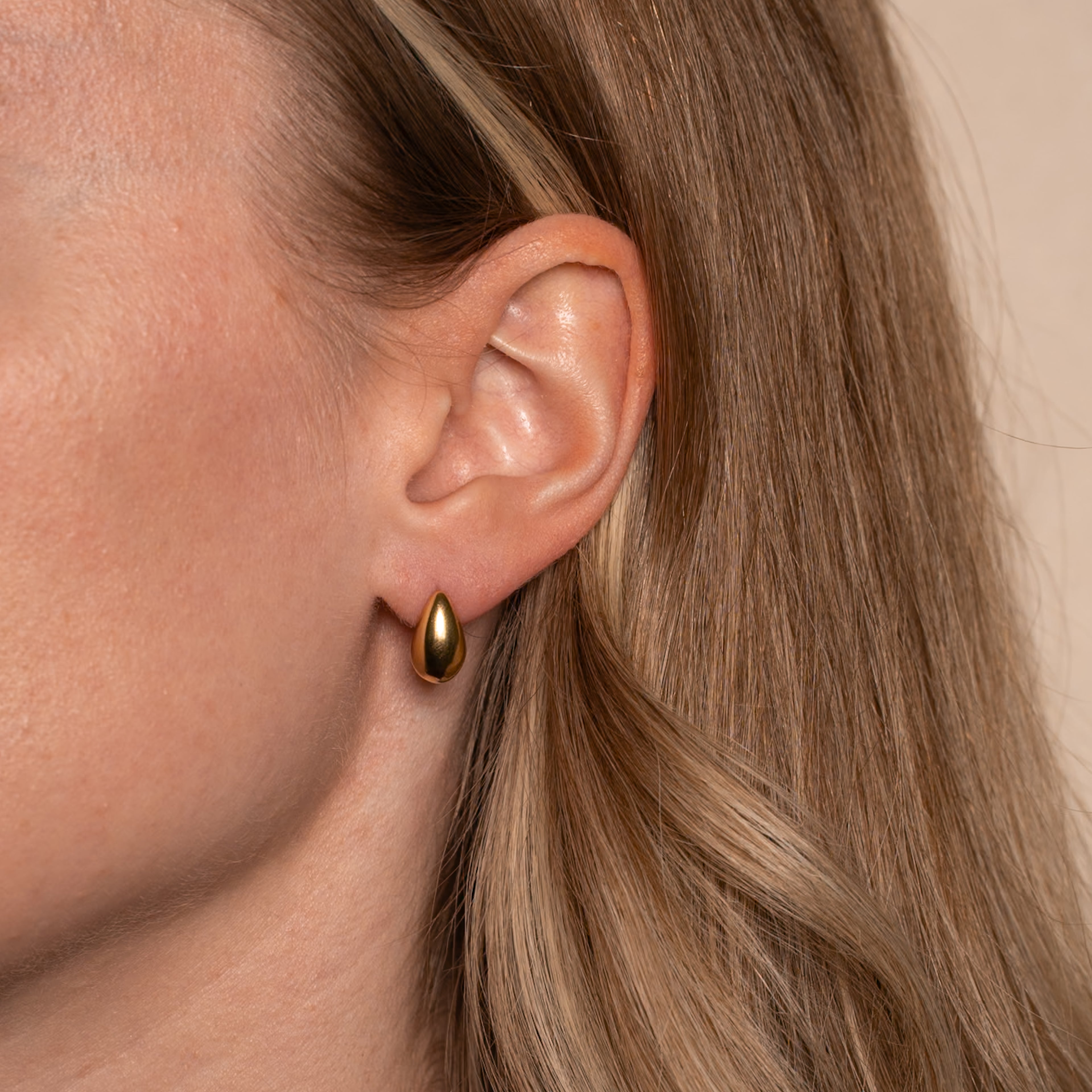 Frau trägt Aria Ohrstecker in gold mit simpler Tropfenform an ihrem Ohr.