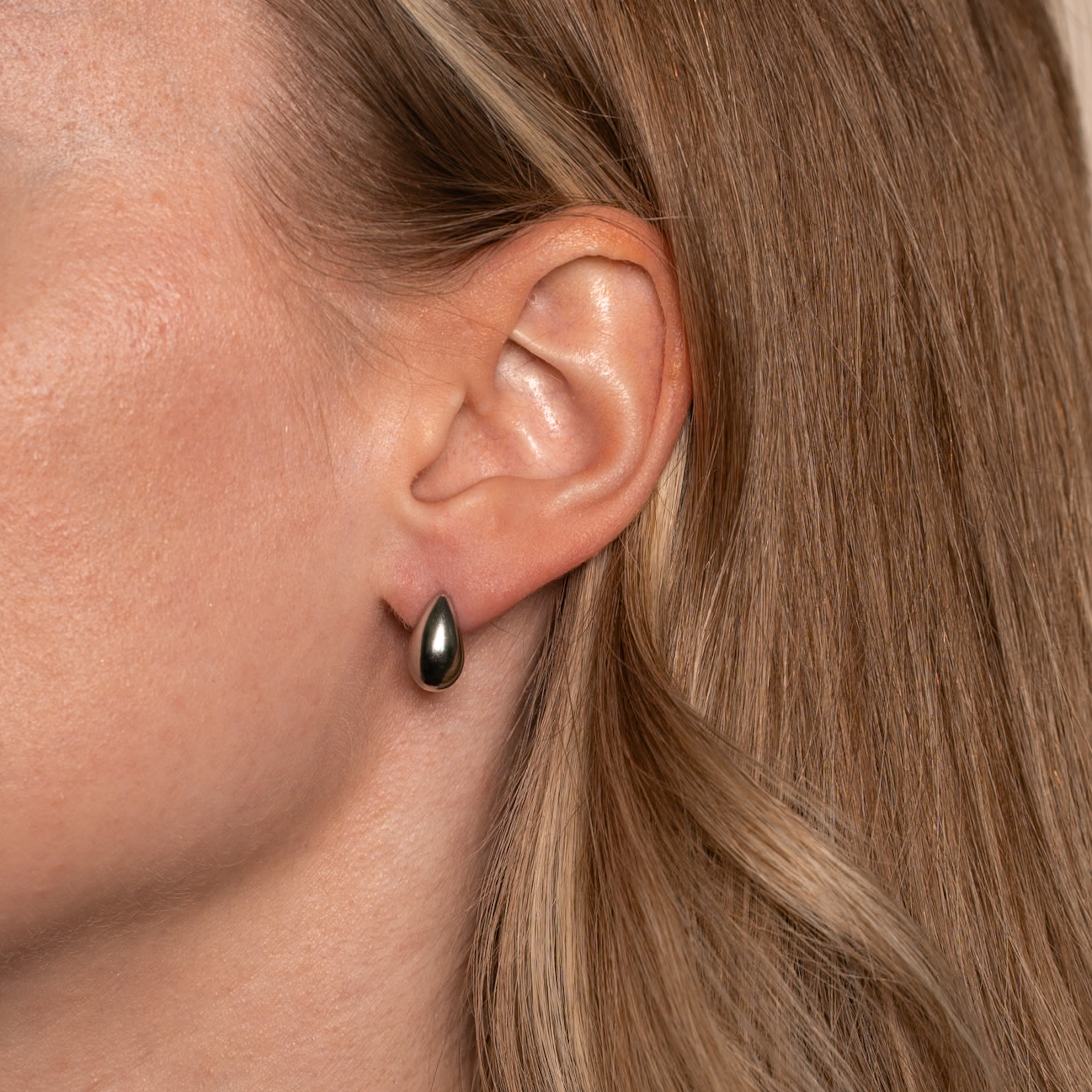 Frau trägt Aria Ohrstecker in silber mit simpler Tropfenform an ihrem Ohr.