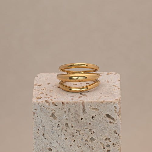 Aurelis Ring in gold mit drei reihen aus glatt poliertem Edelstahl, liegend auf einem Stein.