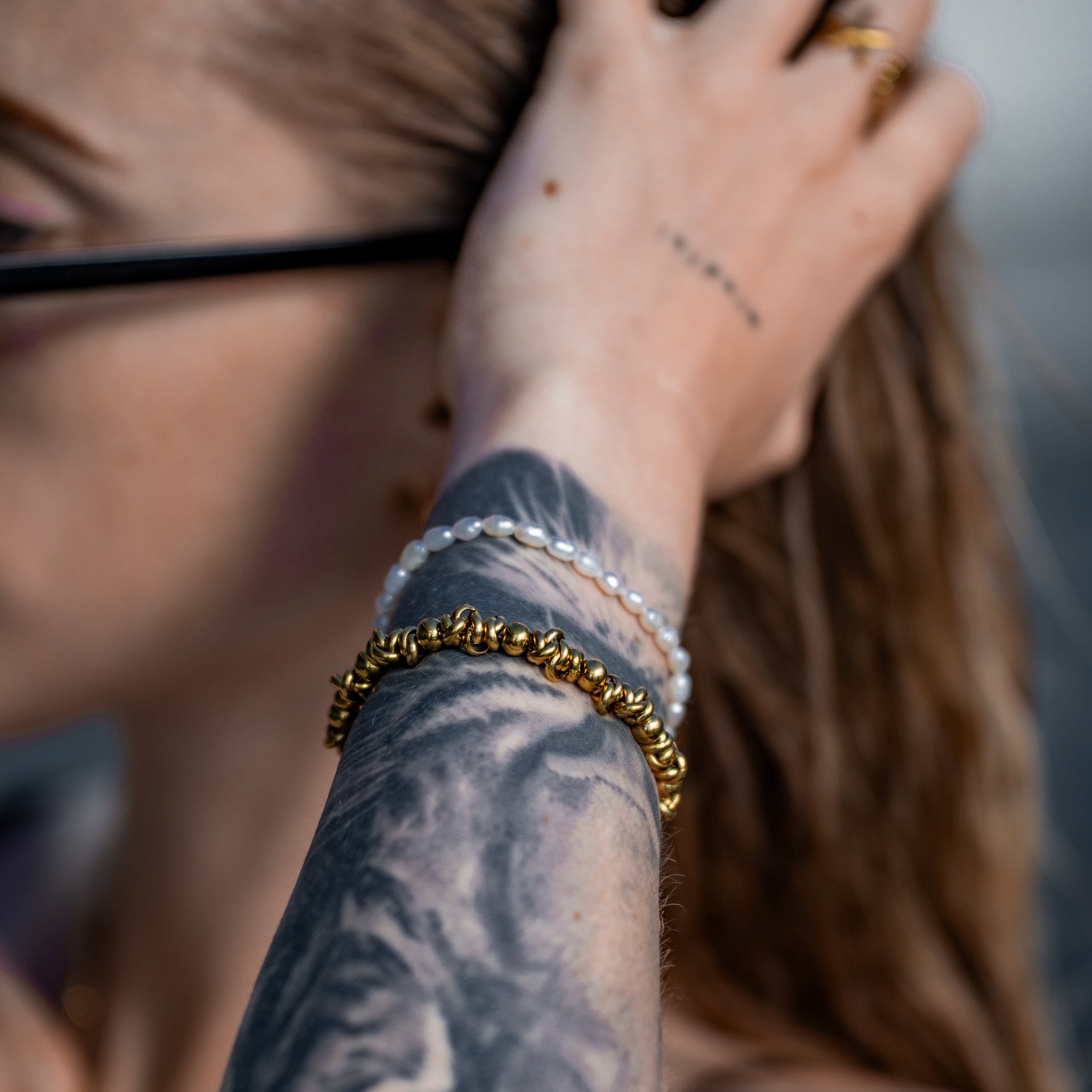 Eos Armband in gold mit vielen unterschiedlich breiten Ringen aus Edelstahl, getragen an einer Frau.