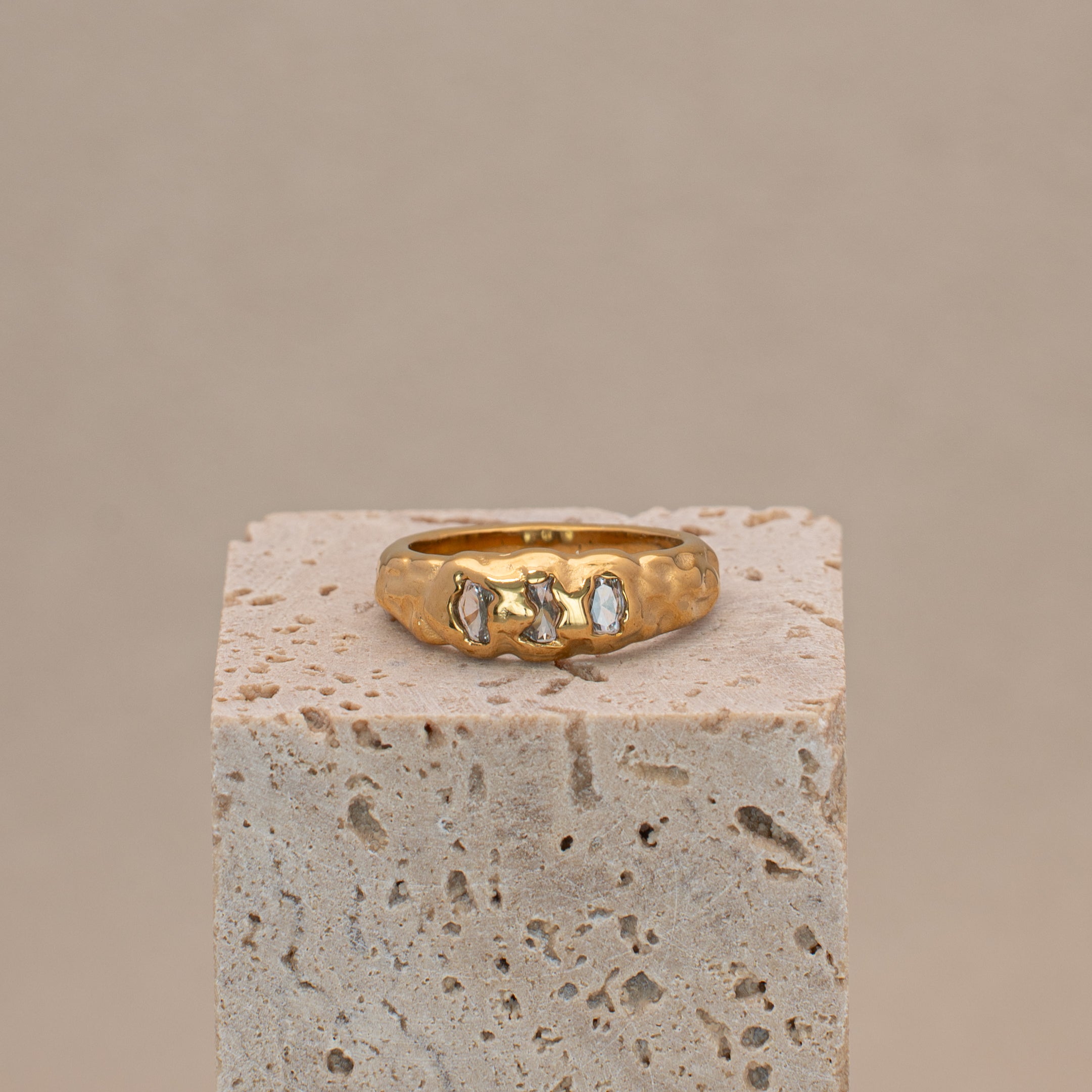 Gaia Ring in gold mit organischer Oberfläche und drei eingefassten Steinen, liegend auf einem Display.