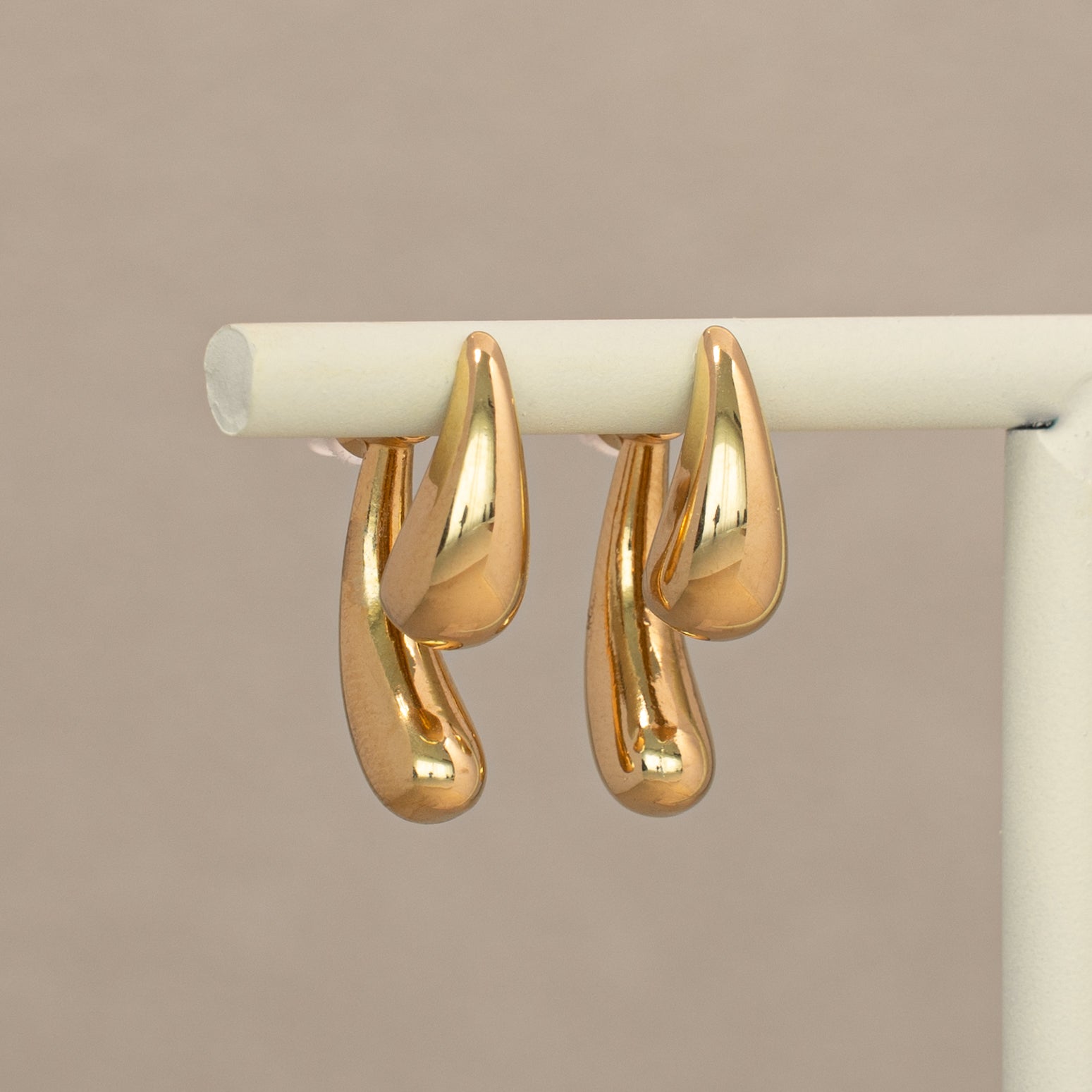 Kuro Ohrstecker in gold mit zwei glatten Tropfen, hängend an einem Display.