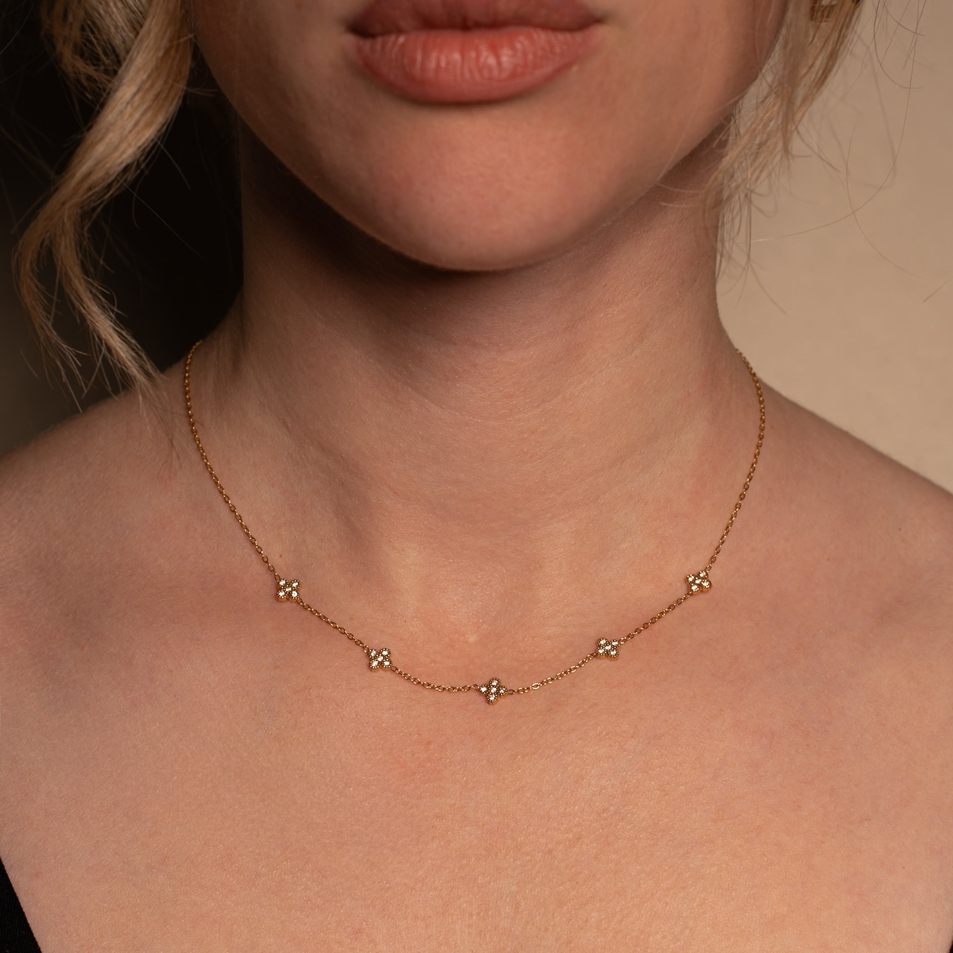 Liana Halskette in gold mit einer filigranen Kette und fünf eingereihten mit Steinen besetzten Kleeblättern, getragen von einer Frau.