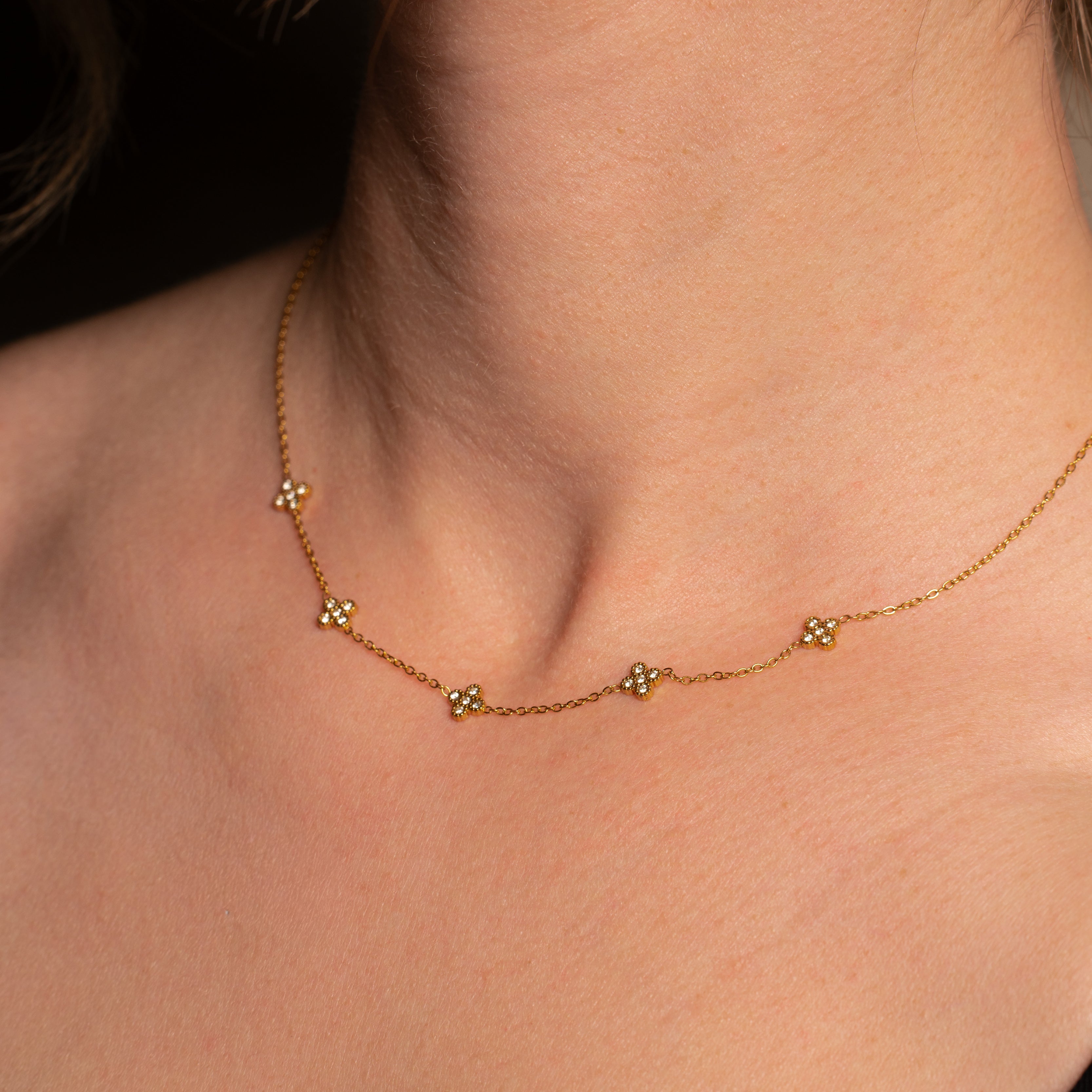 Liana Halskette in gold mit einer filigranen Kette und fünf eingereihten mit Steinen besetzten Kleeblättern, getragen von einer Frau.