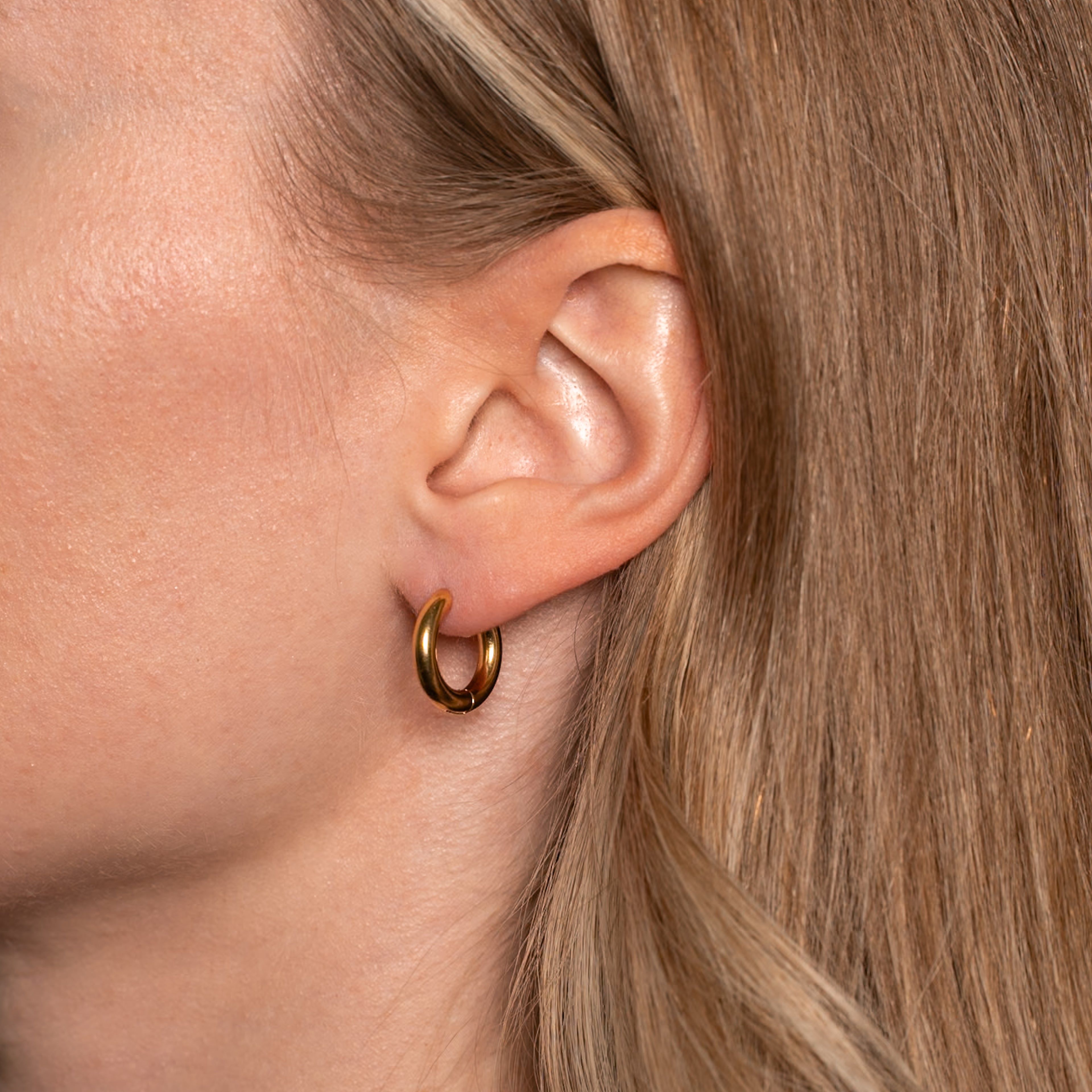 Frau trägt die Liv Ohrringe in gold, kleine basic Creolen.