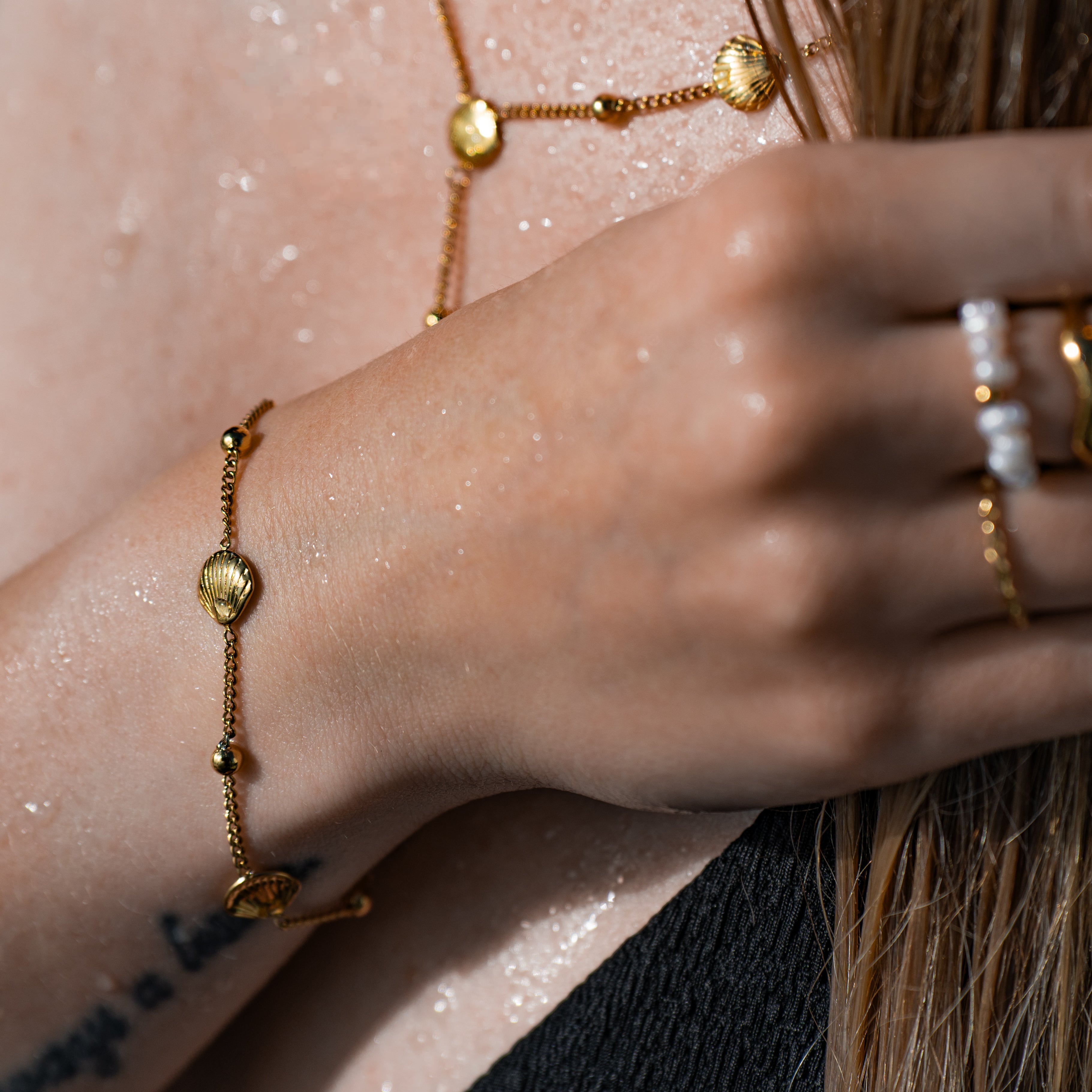 Merida Armband in gold mit einer filigranen Kette und Muscheln komplett aus Edelstahl, getragen an einer Frau.
