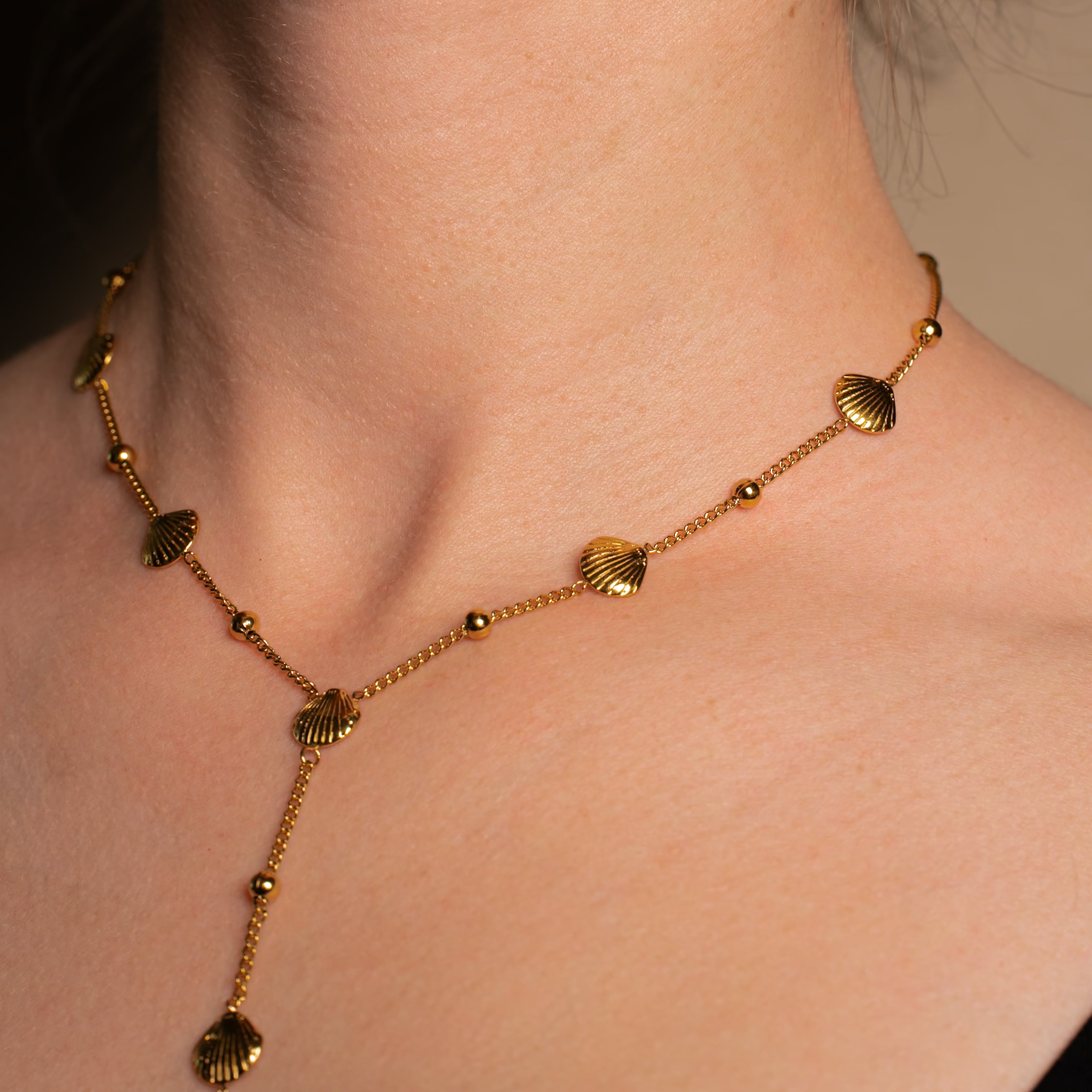 Merida Halskette in gold, Kette in Y-Form mit kleinen Kugeln und Muscheln aus Edelstahl, getragen von einer Frau.