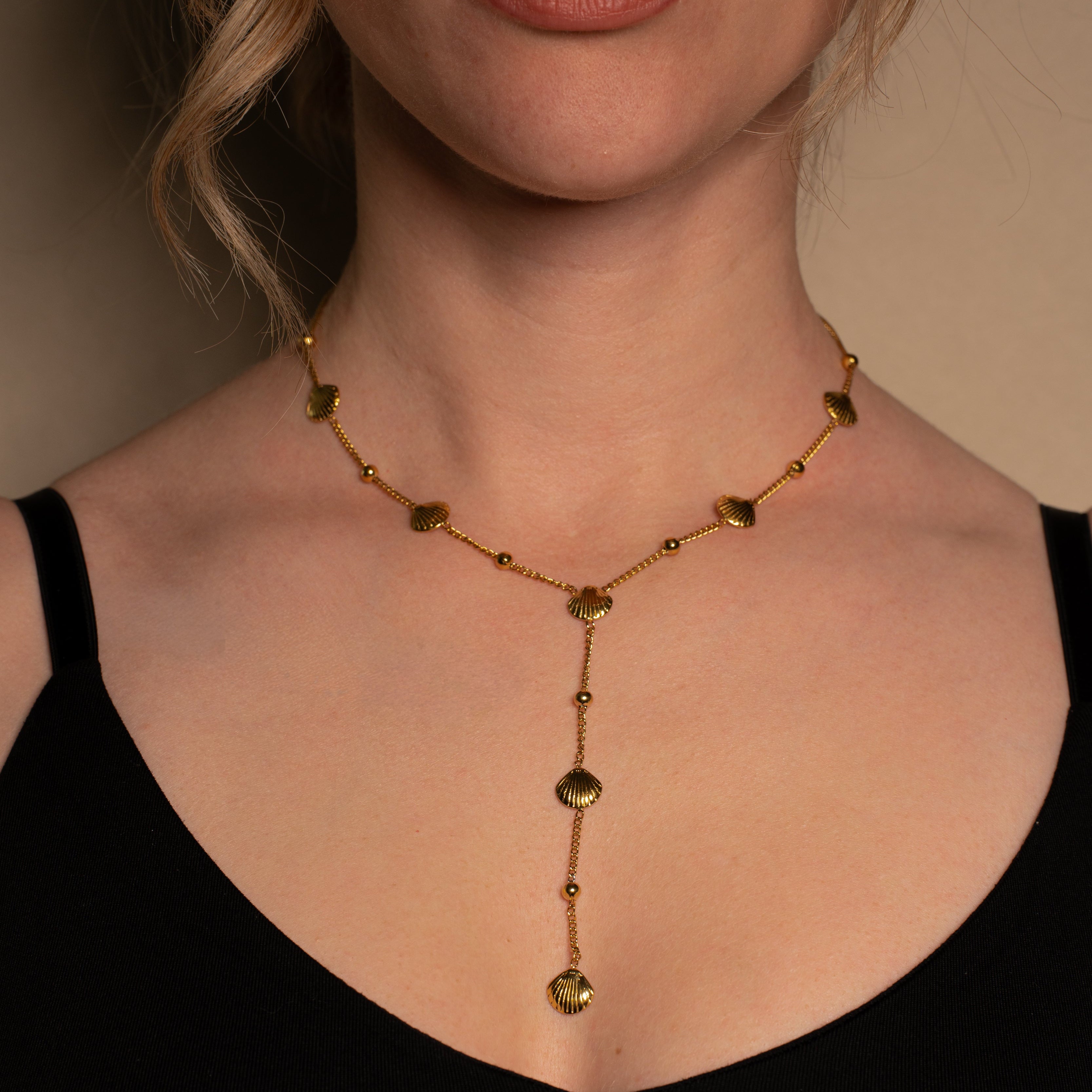Merida Halskette in gold, Kette in Y-Form mit kleinen Kugeln und Muscheln aus Edelstahl, getragen von einer Frau.