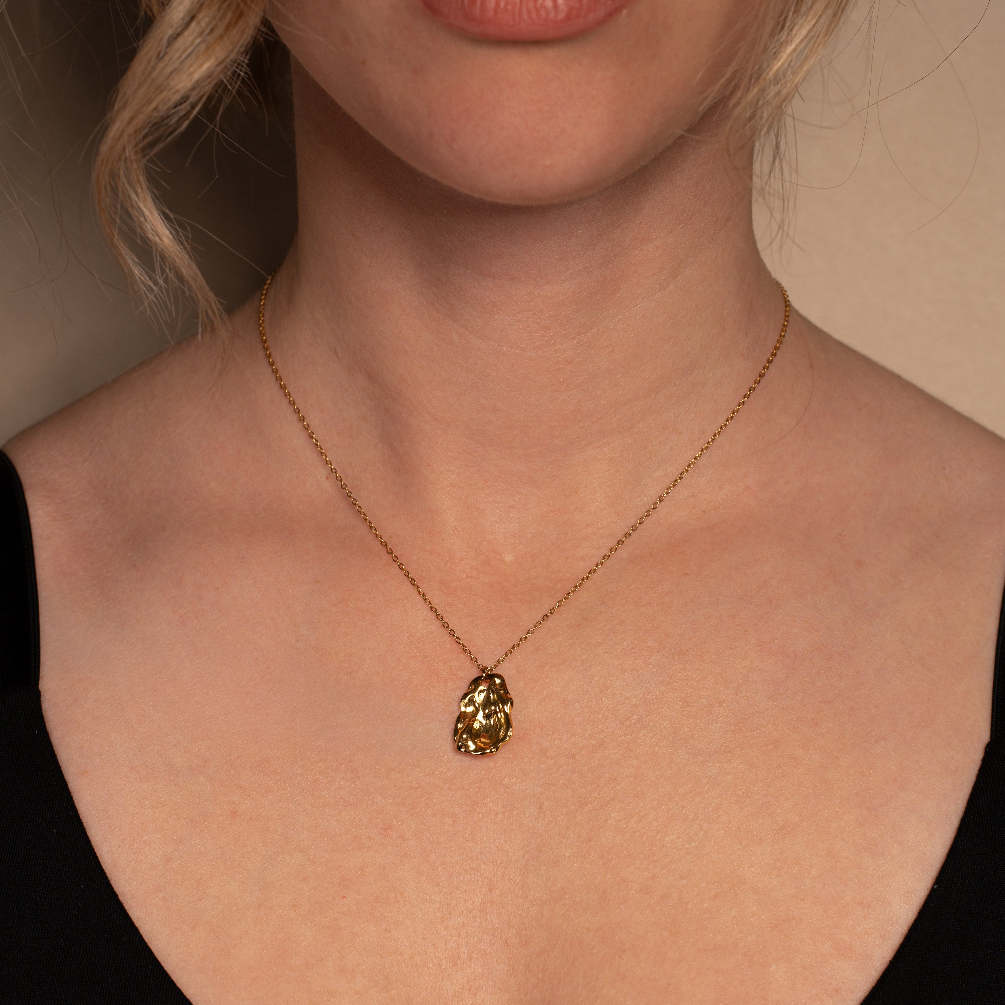 Molten Halskette in gold mit einer filigranen Kette und einem organisch geformten Anhänger, getragen von einer Frau.