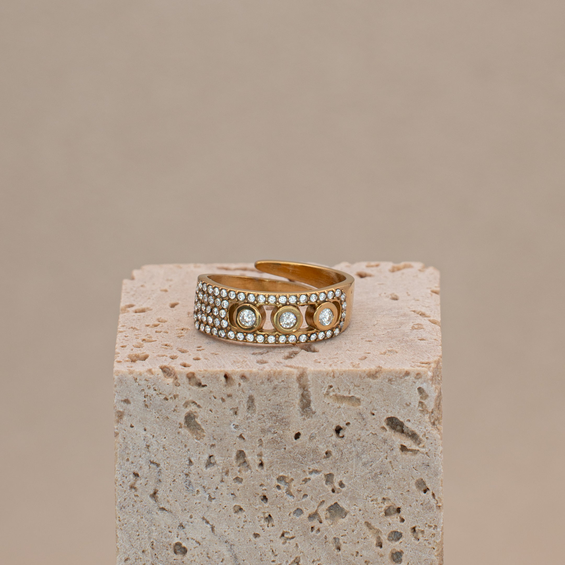 Noelle Ring in Gold, mit Steinen besetztes Band mit drei grösseren Steinen in der Mitte, liegend auf einem Stein.