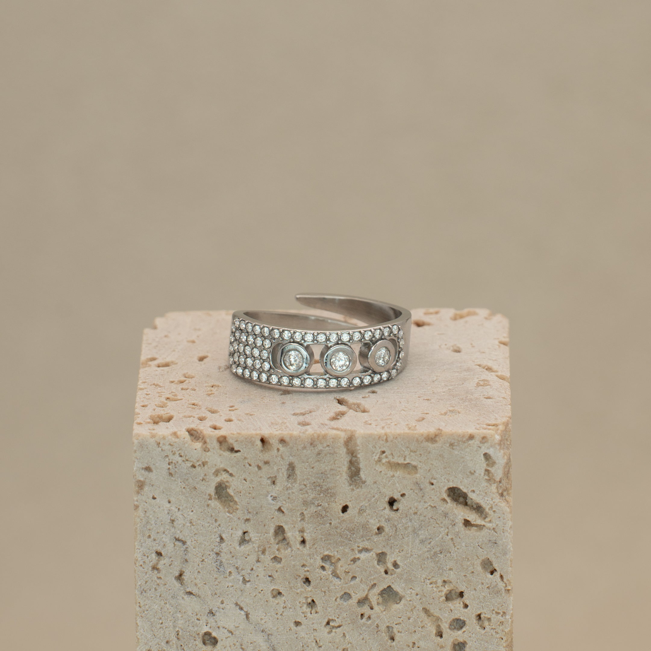 Noelle Ring in silber, mit Steinen besetztes Band mit drei grösseren Steinen in der Mitte, liegend auf einem Stein.