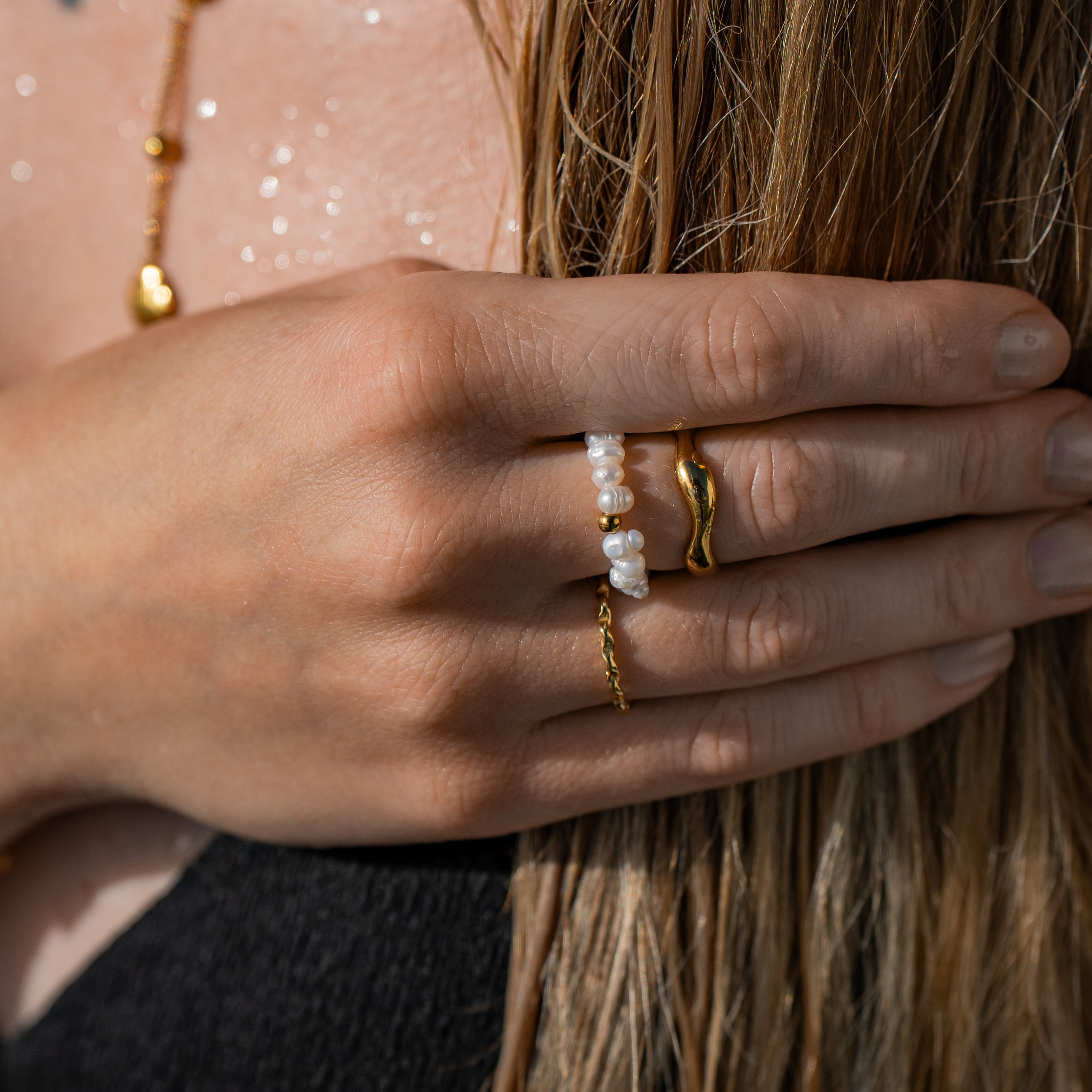 Ring aus einem Band von Süsswasserperlen und einer goldfarbenen Perle aus Edelstahl, getragen an einer Hand.
