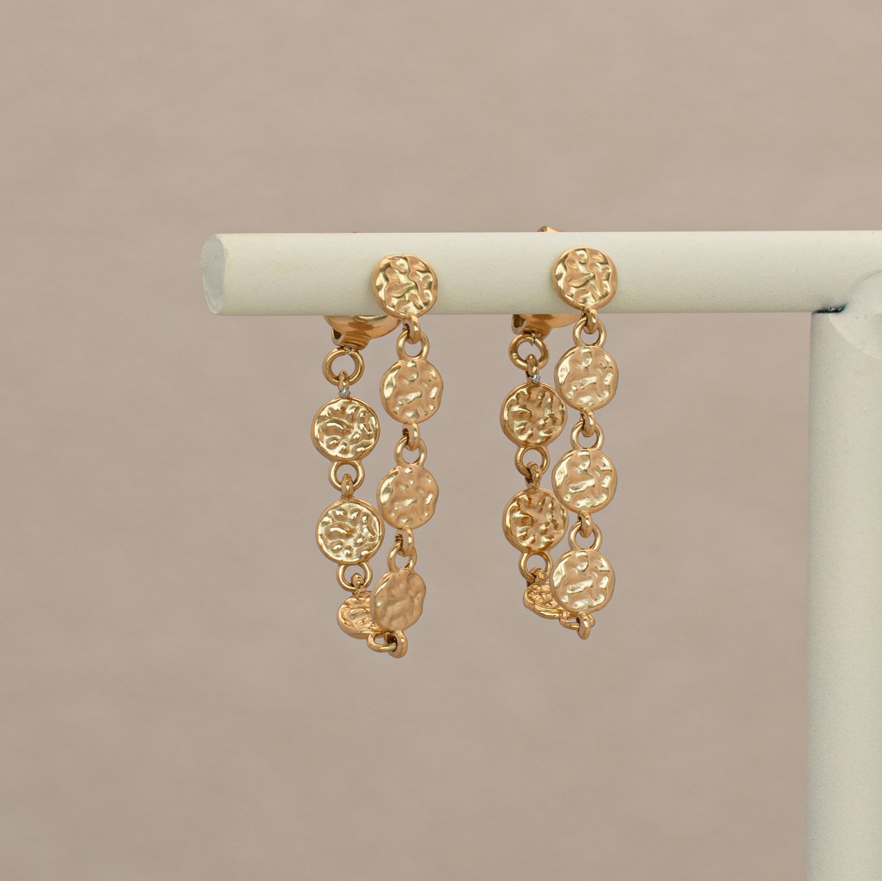Rumi Ohrringe in gold, Creolen bestehend aus einer Kette mit unregelmässigen kleinen Scheiben. Hängend an einem Display.
