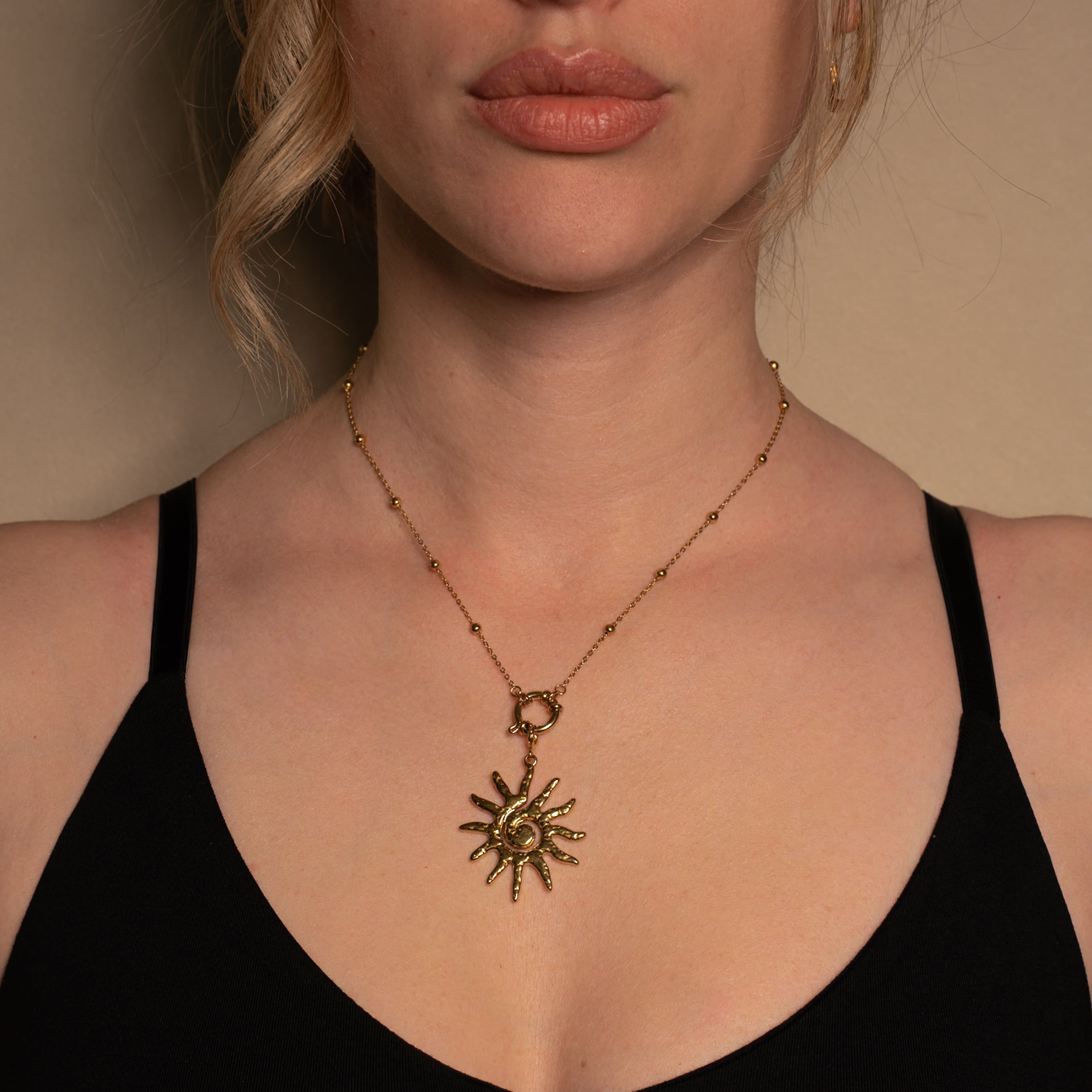 Sol Halskette in gold mit Kugeln und einem Sonnen-Anhänger, getragen von einer Frau.